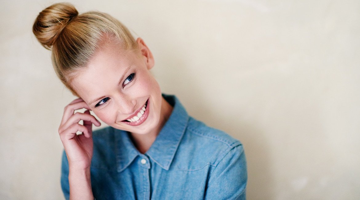 Junge Frau hält Kopf schräg mit zum Dutt gebundene blonden Haaren